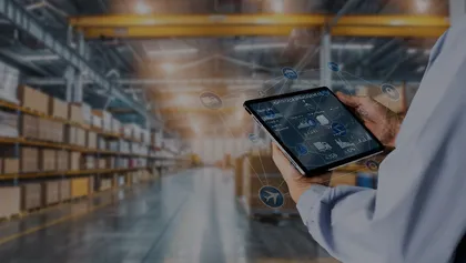 Pessoa a utilizar um tablet com interface digital sobreposta, num armazém moderno cheio de prateleiras com caixas, simbolizando a gestão digital da cadeia de abastecimento.
