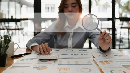 persona sentada frente a varios documentos con gráficos y estadísticas, sostiene una lupa