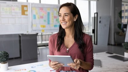 mujer profesional feliz de pie en la oficina, sostiene una tableta y mira al infinito