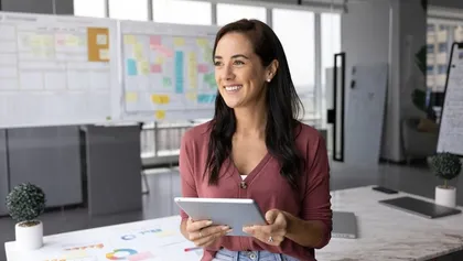mujer profesional feliz de pie en la oficina, sostiene una tableta y mira al infinito
