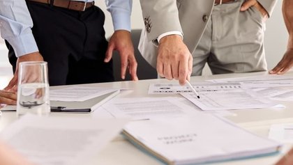 varios hombres reunidos alrededor de unos documentos que hay sobre una mesa de color claro
