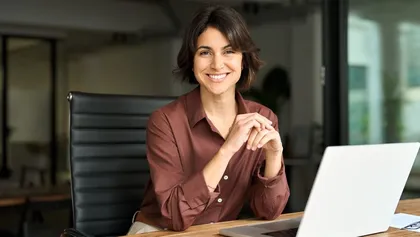 directora de banco sonriente, sentada y con los codos apoyados sobre el escritorio