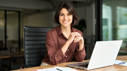 directora de banco sonriente, sentada y con los codos apoyados sobre el escritorio