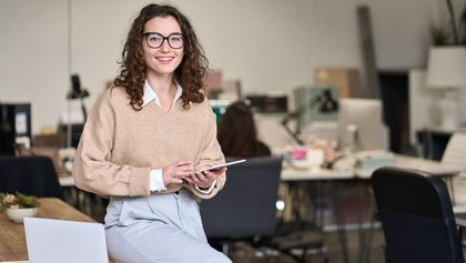 gestora comercial apoyada en una mesa, mientras sostiene una tablet
