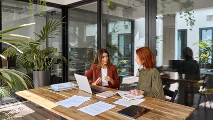 auxiliar administrativa y gerente mantienen una conversación de trabajo, mientras usan un ordenador portátil