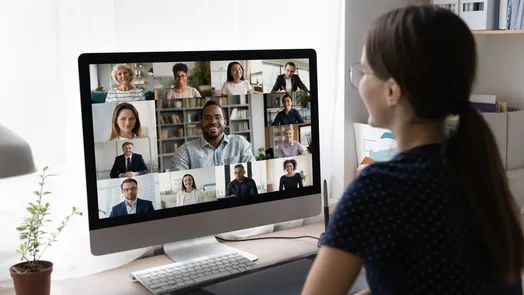 Pessoa a participar numa videoconferência, visível num ecrã de computador com várias pessoas em pequenas janelas de vídeo.