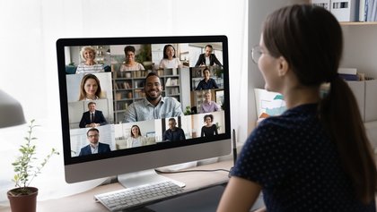 Pessoa a participar numa videoconferência, visível num ecrã de computador com várias pessoas em pequenas janelas de vídeo.