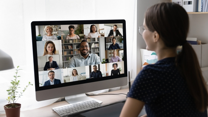 Pessoa a participar numa videoconfer&ecirc;ncia, vis&iacute;vel num ecr&atilde; de computador com v&aacute;rias pessoas em pequenas janelas de v&iacute;deo.