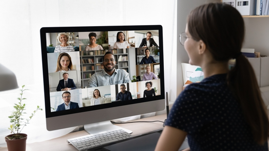 Pessoa a participar numa videoconferência, visível num ecrã de computador com várias pessoas em pequenas janelas de vídeo.